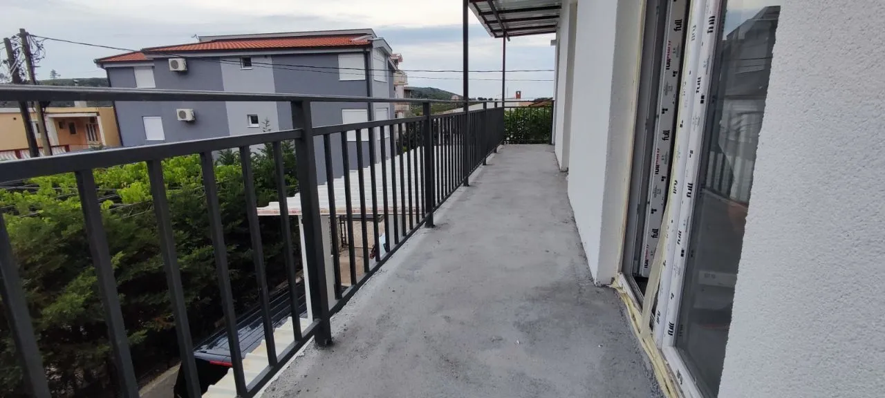 Long balcony with a metal railing and a view of surrounding buildings and greenery.