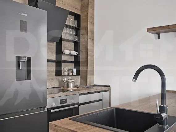Modern kitchen with wood-grain cabinetry, black refrigerator, and built-in oven.