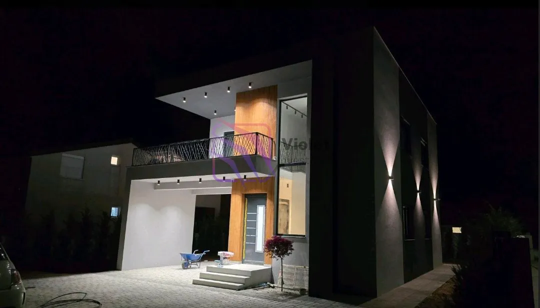 Noćni pogled na spoljašnjost moderne kuće sa osvetljenjem i terasom.