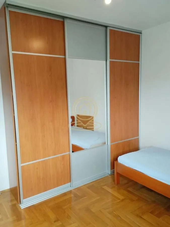 Spavaća soba sa drvenim krevetom i velikim ugradnim garderoberom sa ogledalom.