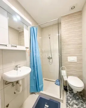 Compact bathroom equipped with a washbasin, a shower cabin with a blue curtain, and a toilet. - image 7