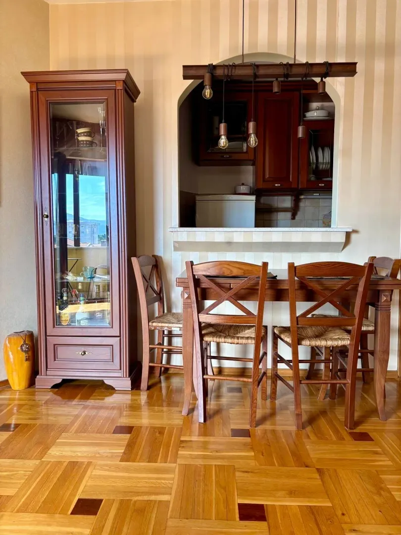 Dining area with a wooden table, chairs, and a display cabinet, with a view of part of the kitchen.