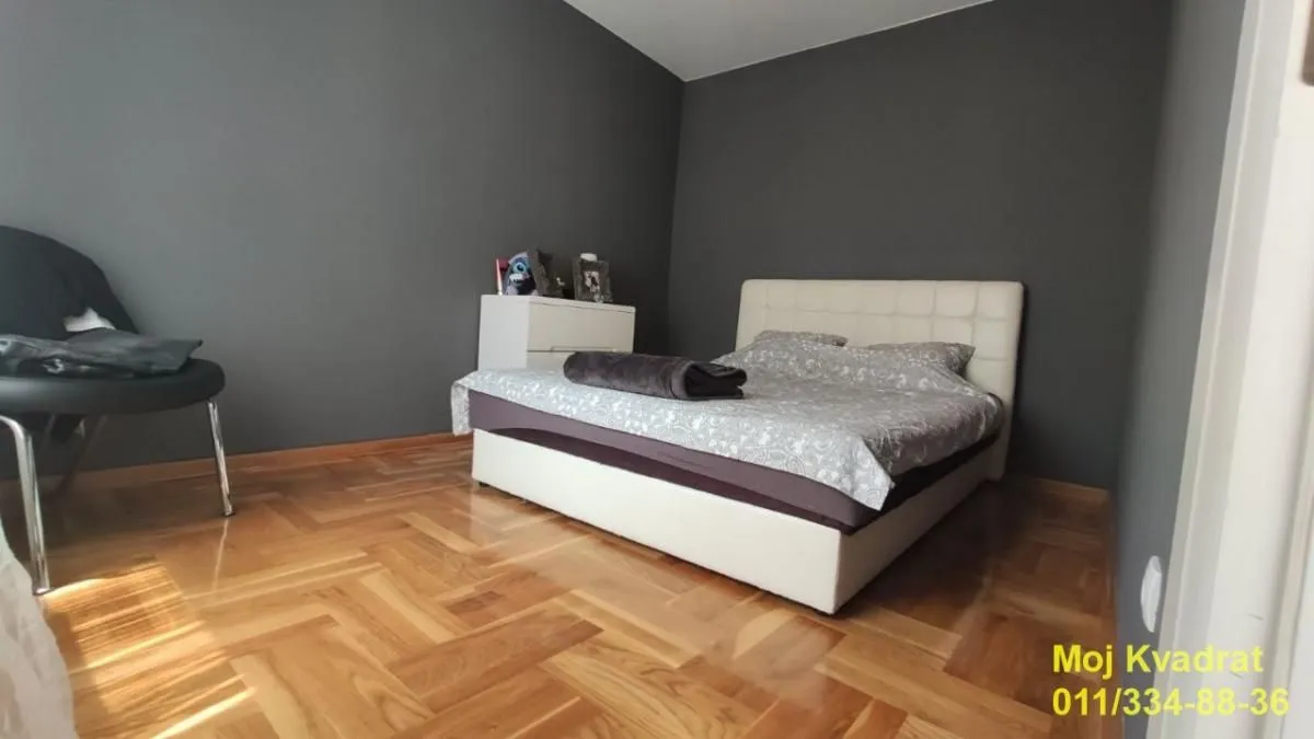 Spavaća soba sa bračnim krevetom, parketom i tamnim zidovima.