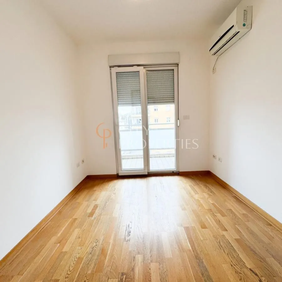Empty room with wooden flooring, air conditioning, and balcony doors.