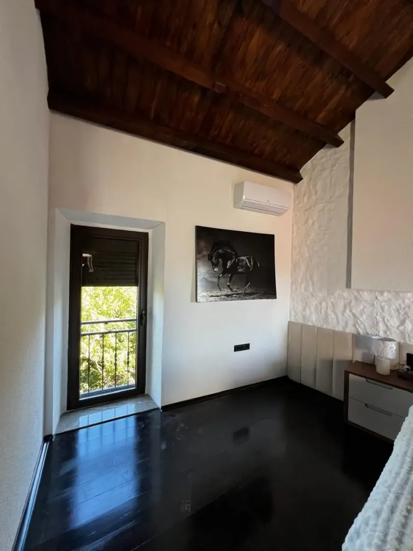 Svijetla spavaća soba sa visokim drvenim plafonom i izlazom na balkon.