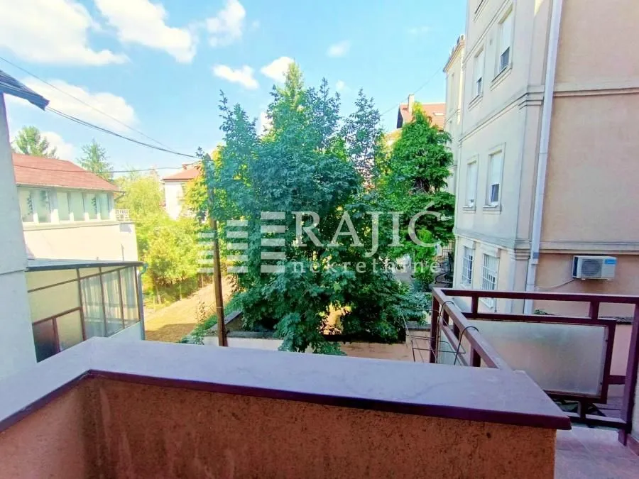 Pogled sa balkona na okolne zgrade i zelenilo.