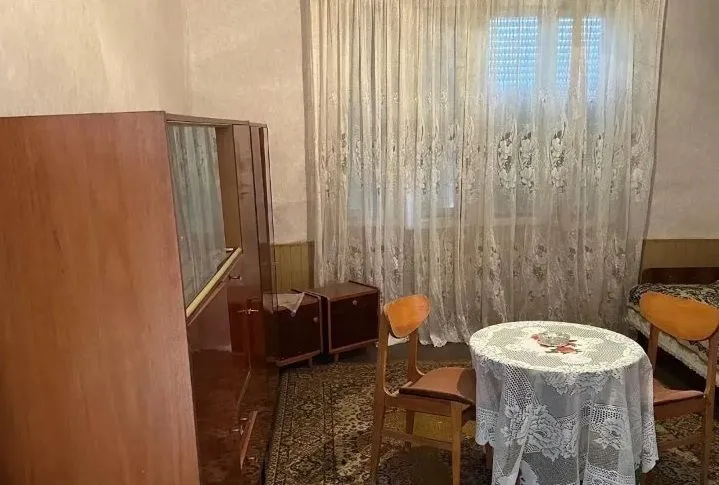 Dnevna soba sa trpezarijskim stolom, starim nameštajem i tepihom.