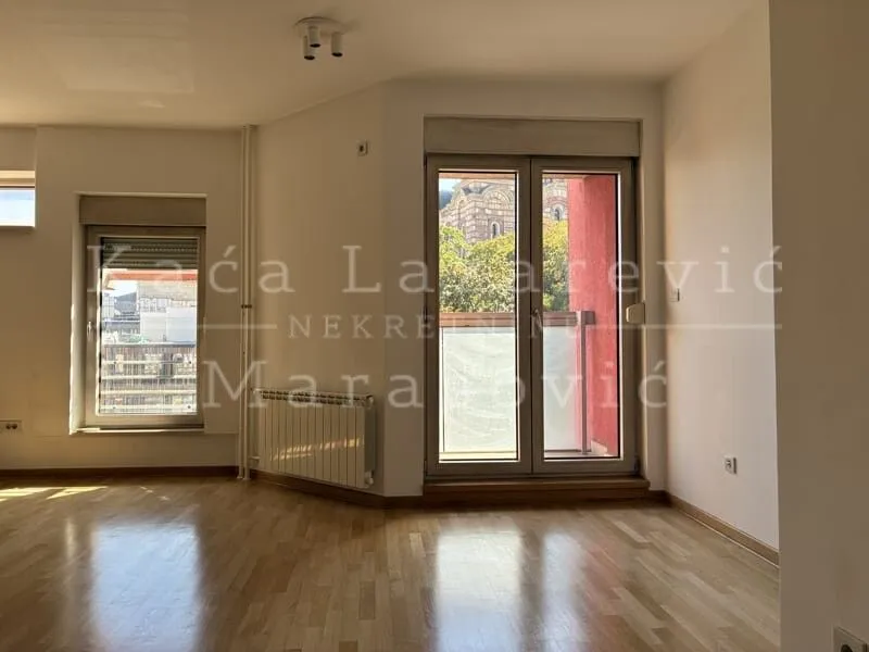 Empty room with wooden flooring, windows, and balcony doors.