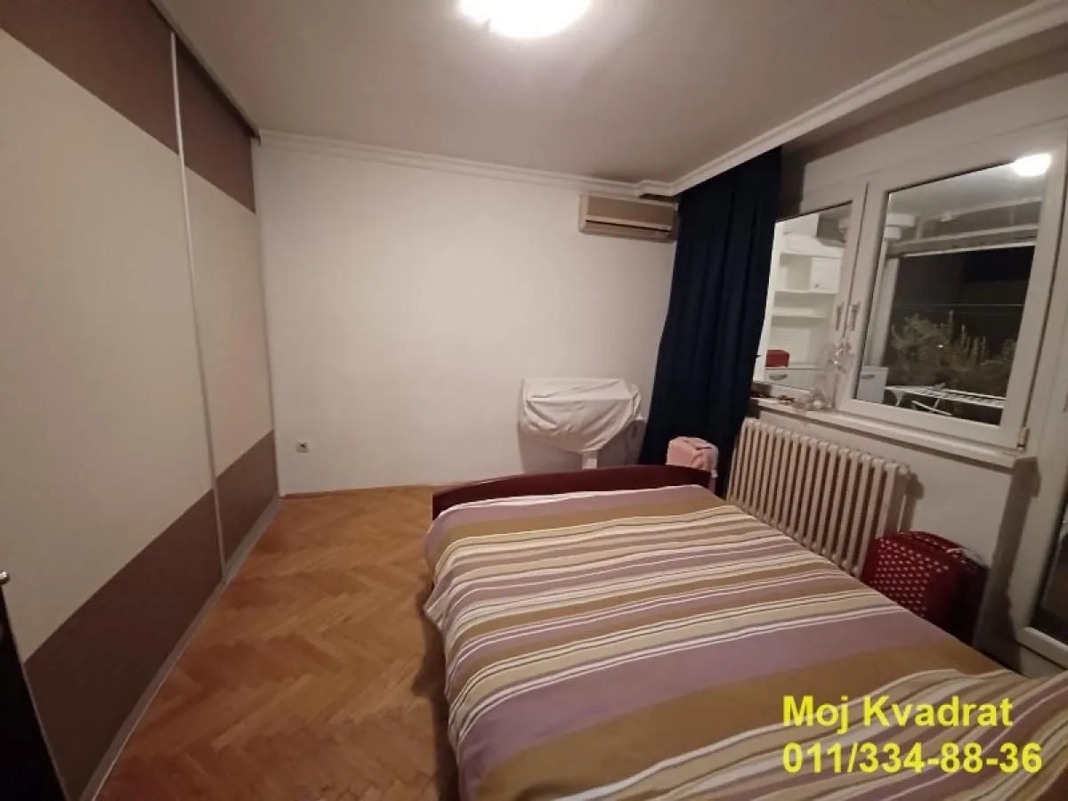 Nameštena spavaća soba sa bračnim krevetom, ormarom i parketom na podu.