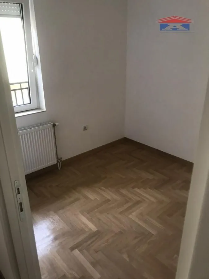 Prazna soba sa parketom i prozorom, gledana sa vrata.