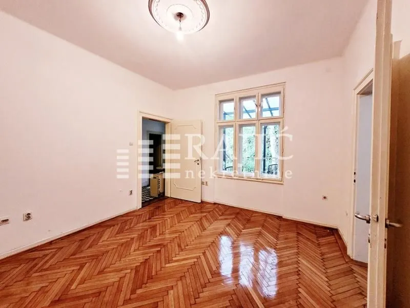Empty room with parquet flooring and a large window.