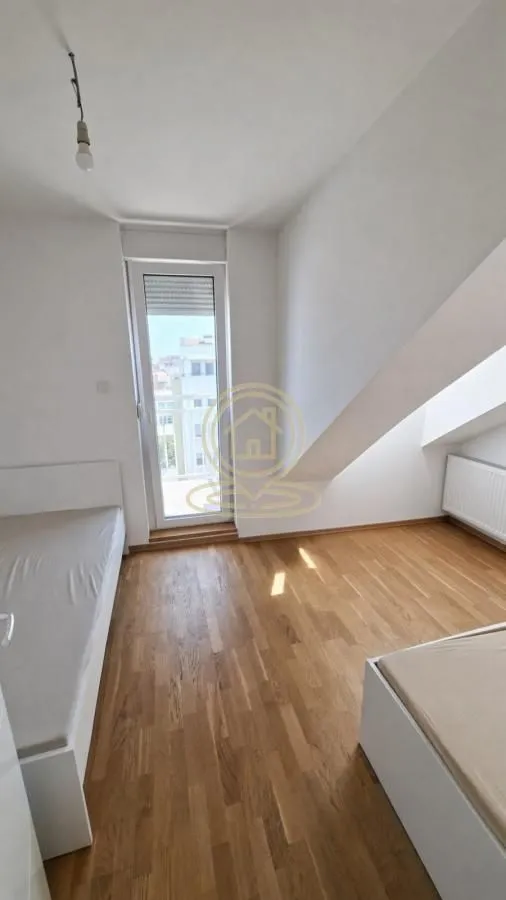 Spavaća soba sa kosinama, drvenim podom i izlazom na terasu.