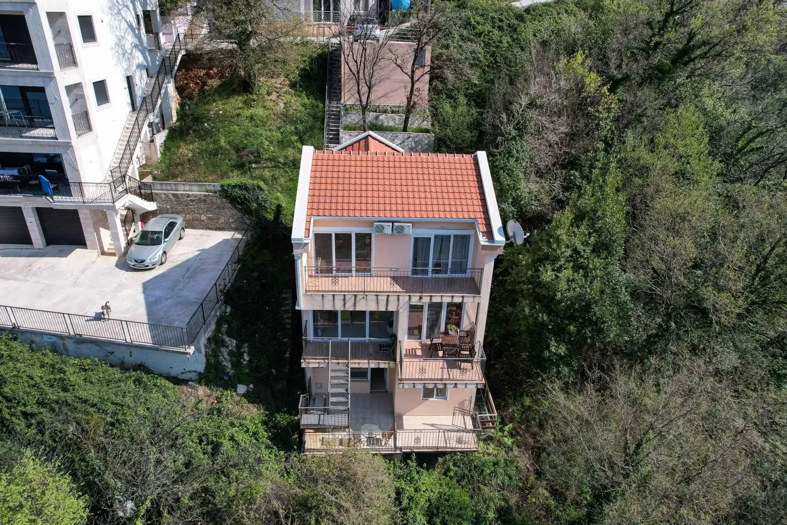 Pogled iz vazduha na višestambenu kuću okruženu zelenilom.