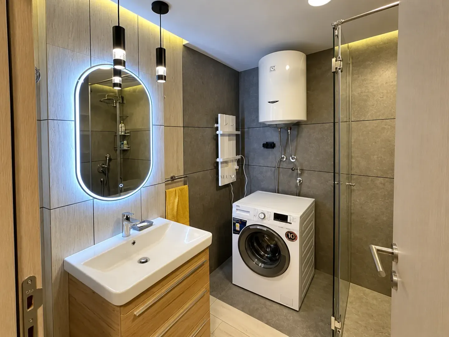 A modern bathroom equipped with a sink, washing machine, water heater, and walk-in shower.