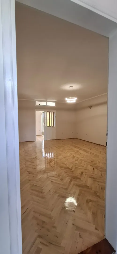 Prazna soba sa parketom i plafonskim osvjetljenjem, gledana kroz vrata.
