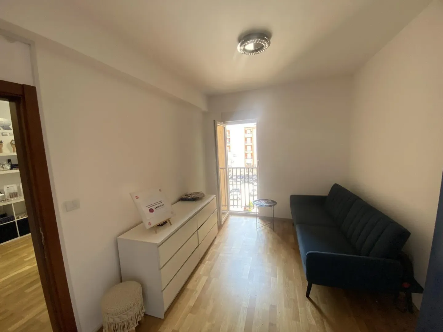 A bright room featuring a dark blue sofa, a white chest of drawers, and access to a small balcony.