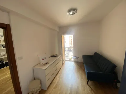 A bright room featuring a dark blue sofa, a white chest of drawers, and access to a small balcony. - image 6