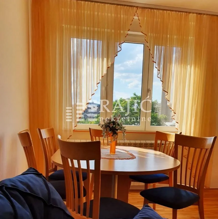 Dining area with wooden table and chairs near a window with yellow curtains.