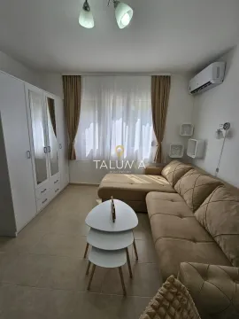 Manja dnevna soba opremljena ugaonom garniturom, bijelim ormarom i malim stočićem. - image 2