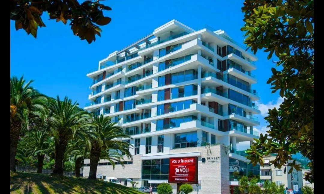 Exterior of a modern multi-family residential building with balconies and surrounding palm trees.