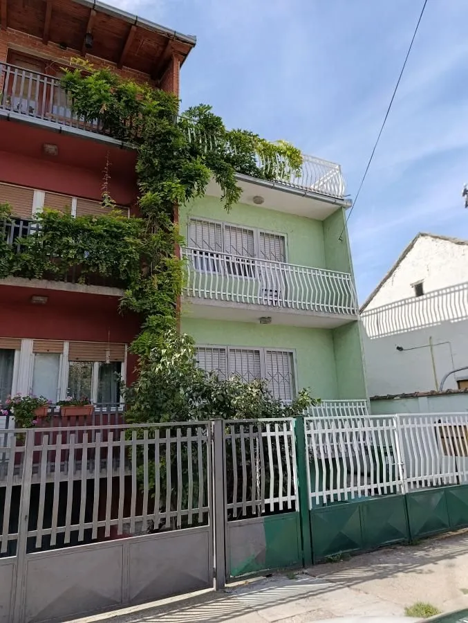 Pogled na spoljašnjost zgrade sa dvorišnom kapijom i zelenilom.