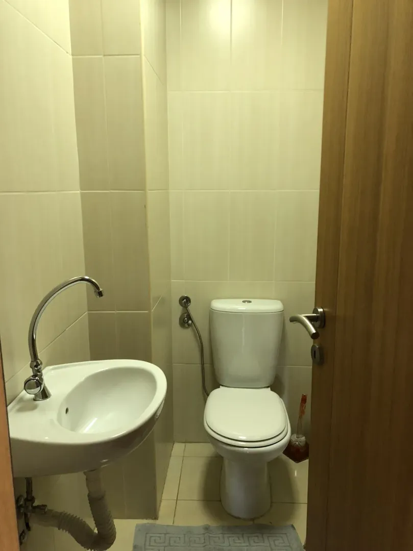 A small bathroom featuring a toilet and a sink with light-colored tiling.