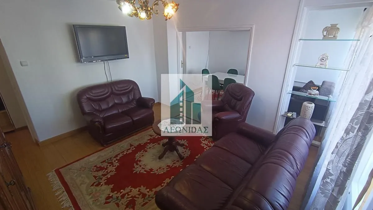 Living room with dark leather sofas, a coffee table, and a wall-mounted TV.