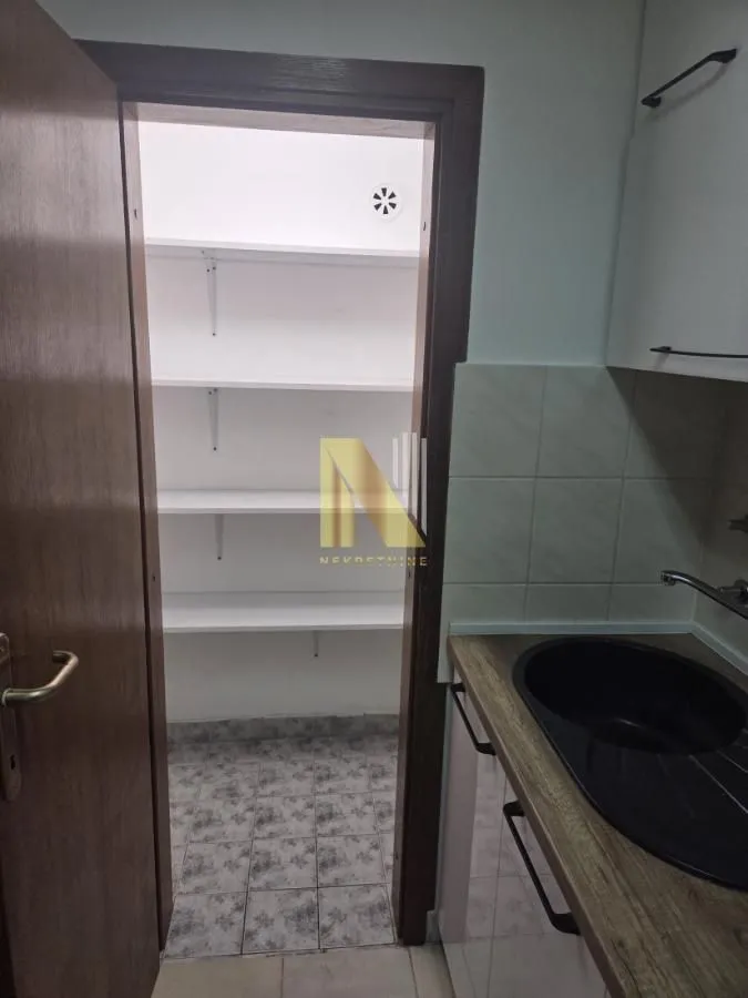 Prikaz dela kuhinje sa sudoperom i pogledom na ostavu sa policama.