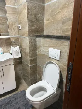 Manje kupatilo sa WC šoljom, umivaonikom i braon keramičkim pločicama. - image 5