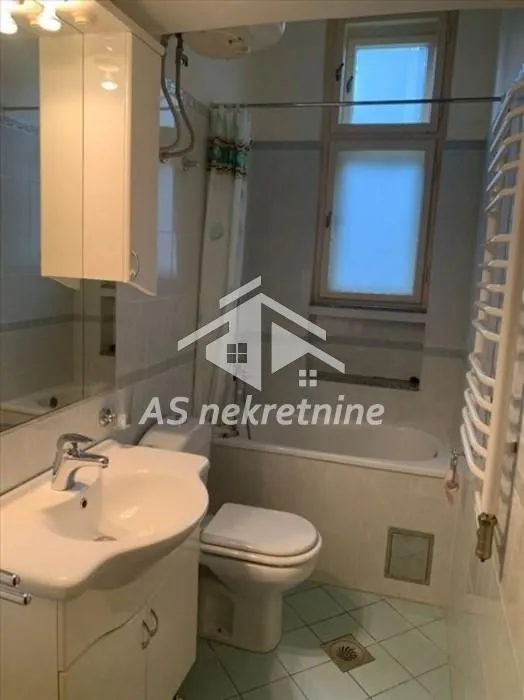 Kupatilo opremljeno sanitarijama, kadom i ormarićem sa ogledalom.
