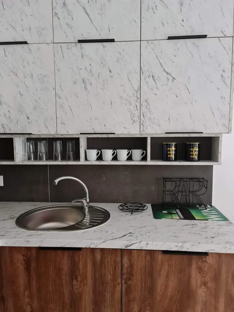 Dio kuhinje sa sudoperom, radnom pločom i gornjim elementima sa dezenom mermera.