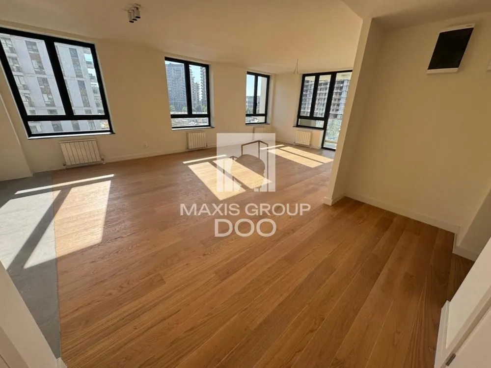 Empty room with wooden flooring and large windows.