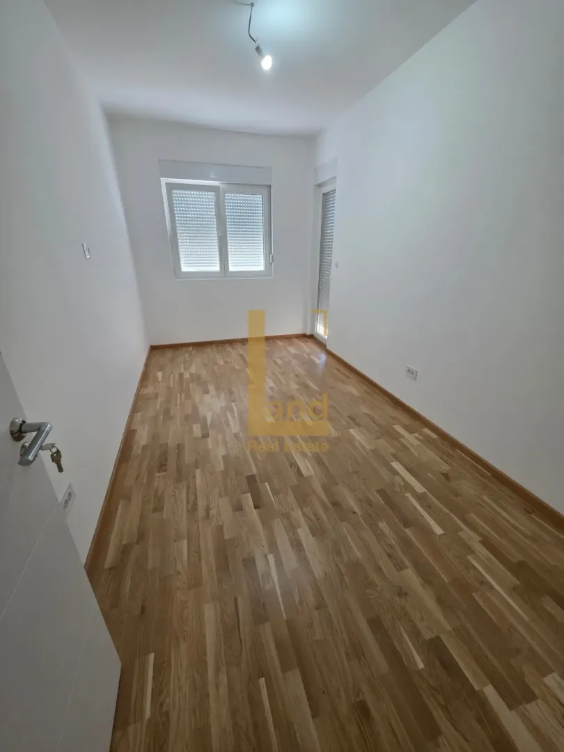 Prazna soba sa parketom i bijelim zidovima.