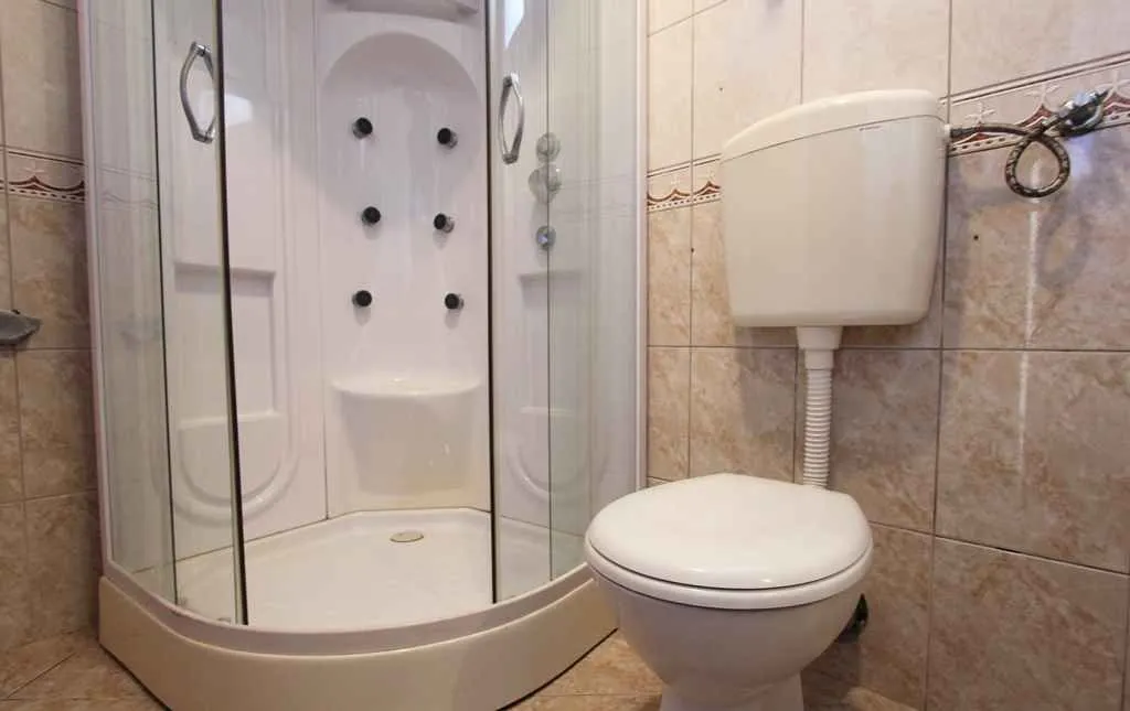 Manje kupatilo sa tuš kabinom i toaletom obloženo keramičkim pločicama.
