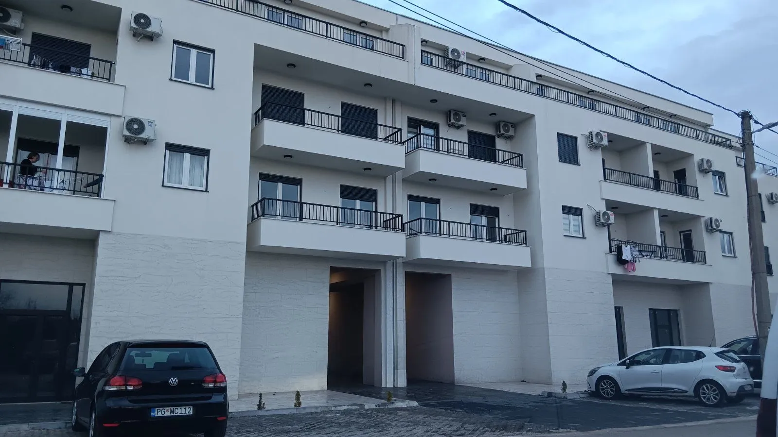 Exterior view of a modern residential building with balconies and parking in front.