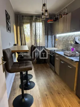 Small kitchen with wooden-pattern cabinetry, built-in appliances, and a bar counter with bar stools. - image 7
