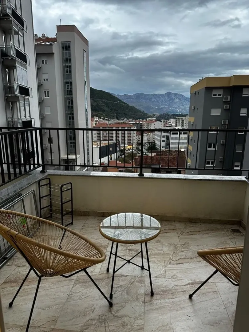 Nenamešten balkon sa garniturom za sjedenje i pogledom na grad i planine.