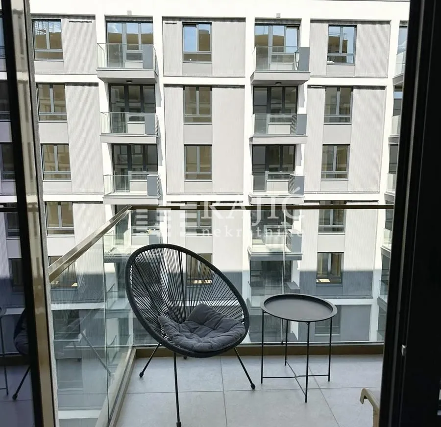 Small furnished balcony with glass railing and view of the building.