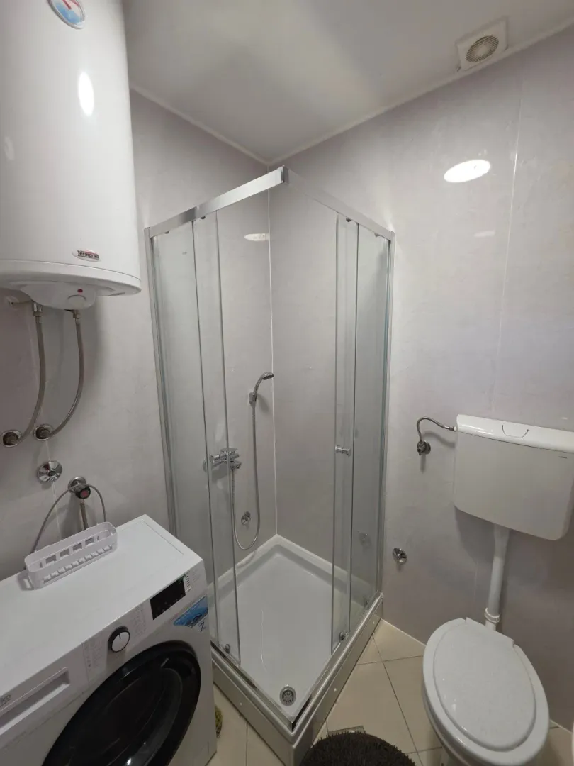 Small bathroom with a shower cabin, toilet, water heater, and washing machine.