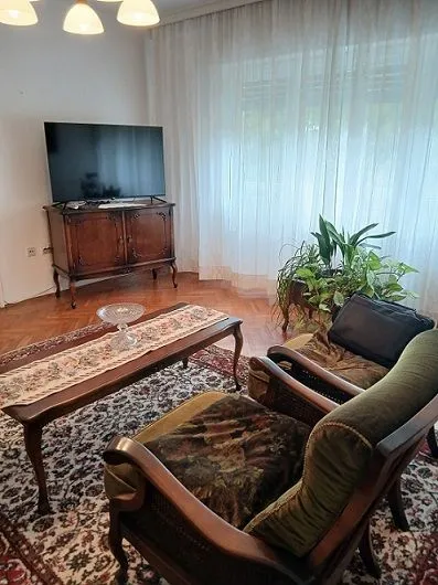 Dnevna soba sa garniturom, televizorom i trpezarijskim stolom.