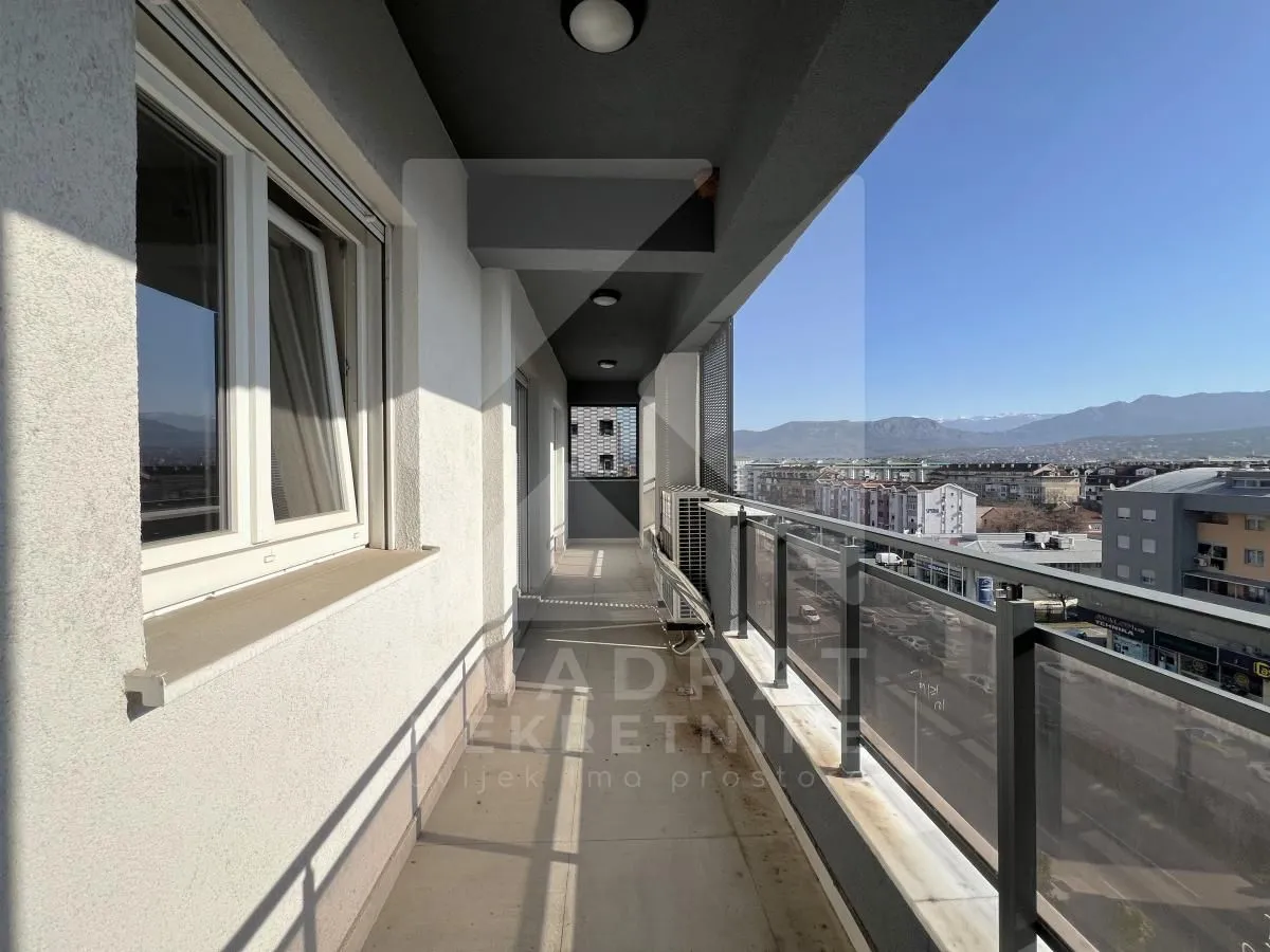 Dugačak natkriveni balkon sa pogledom na grad i planine.