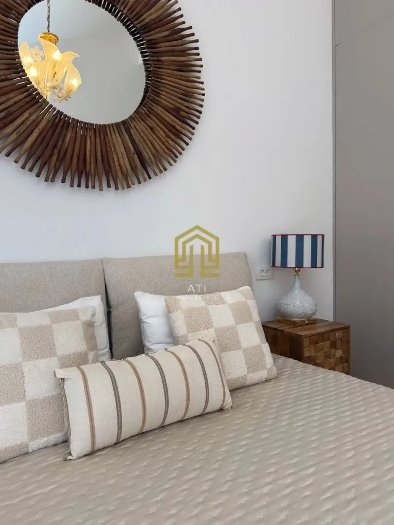 Detail of the bedroom with a bed, decorative pillows, nightstand and a mirror on the wall.