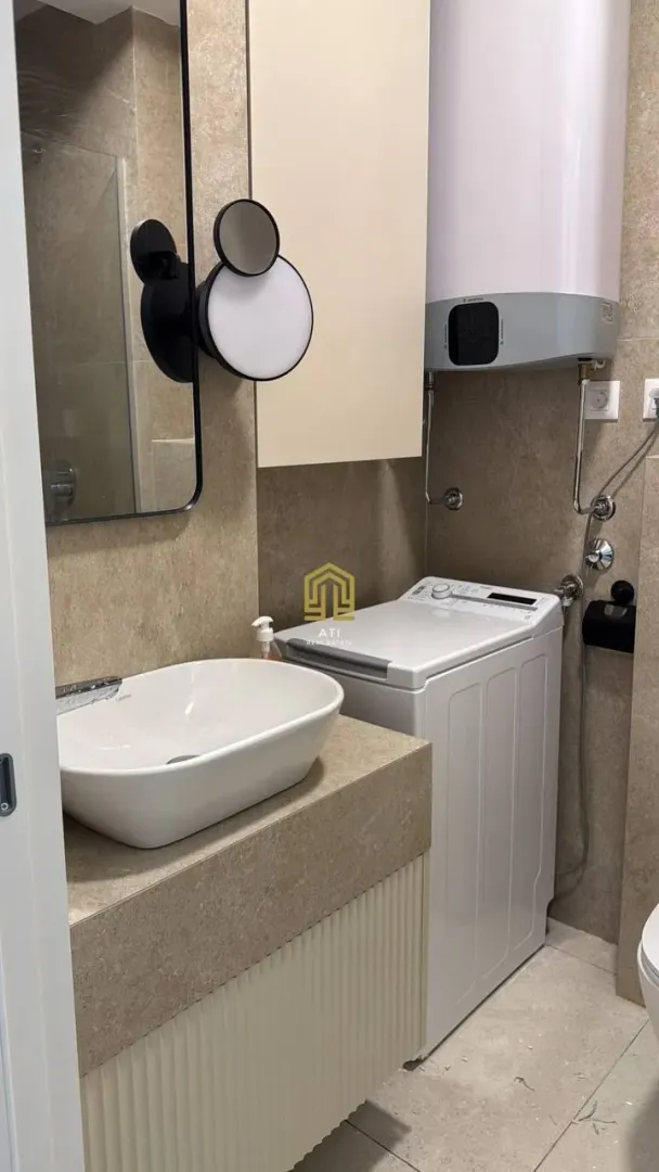 Moderne kupatilo sa umivaonikom, ogledalom i mašinom za veš.