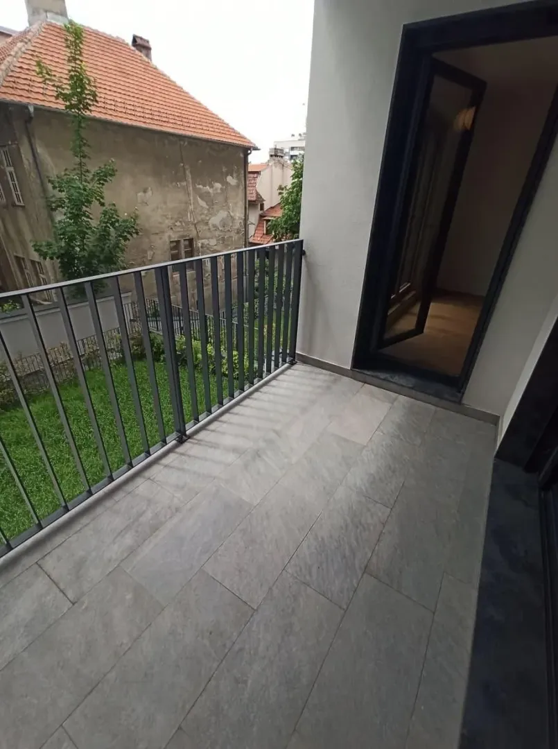 Small tiled balcony with a metal railing and a view of surrounding buildings and a courtyard.