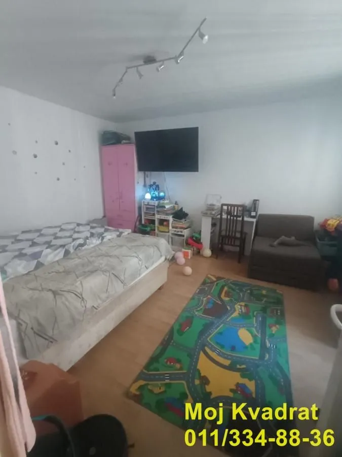 Dečja soba sa krevetom, radnim stolom i TV-om na zidu.