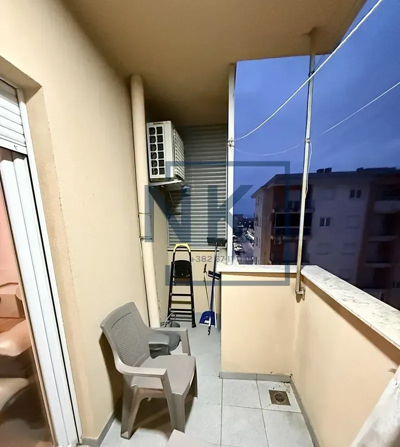 Manji natkriveni balkon sa spoljnom jedinicom klima uređaja i plastičnom stolicom.