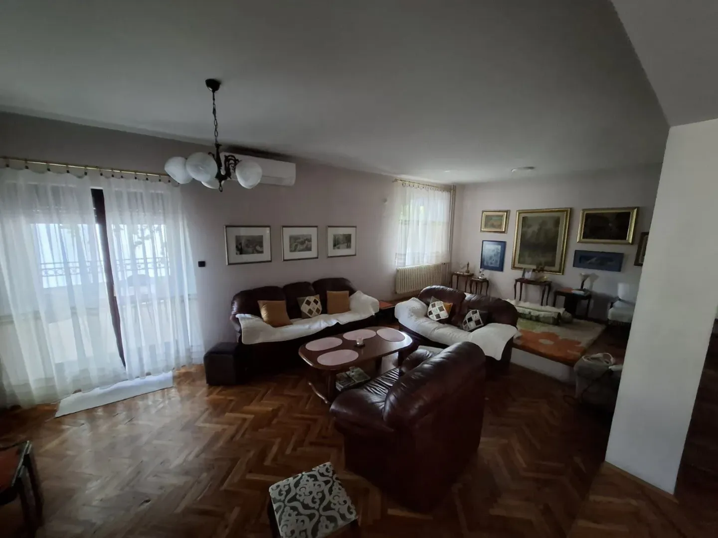 Spacious living room with seating furniture and parquet flooring.