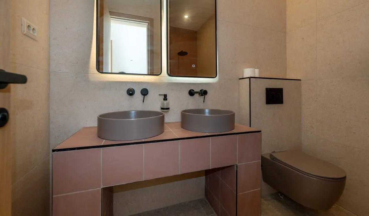 Modern bathroom with double sink, mirrors, and wall-mounted toilet.