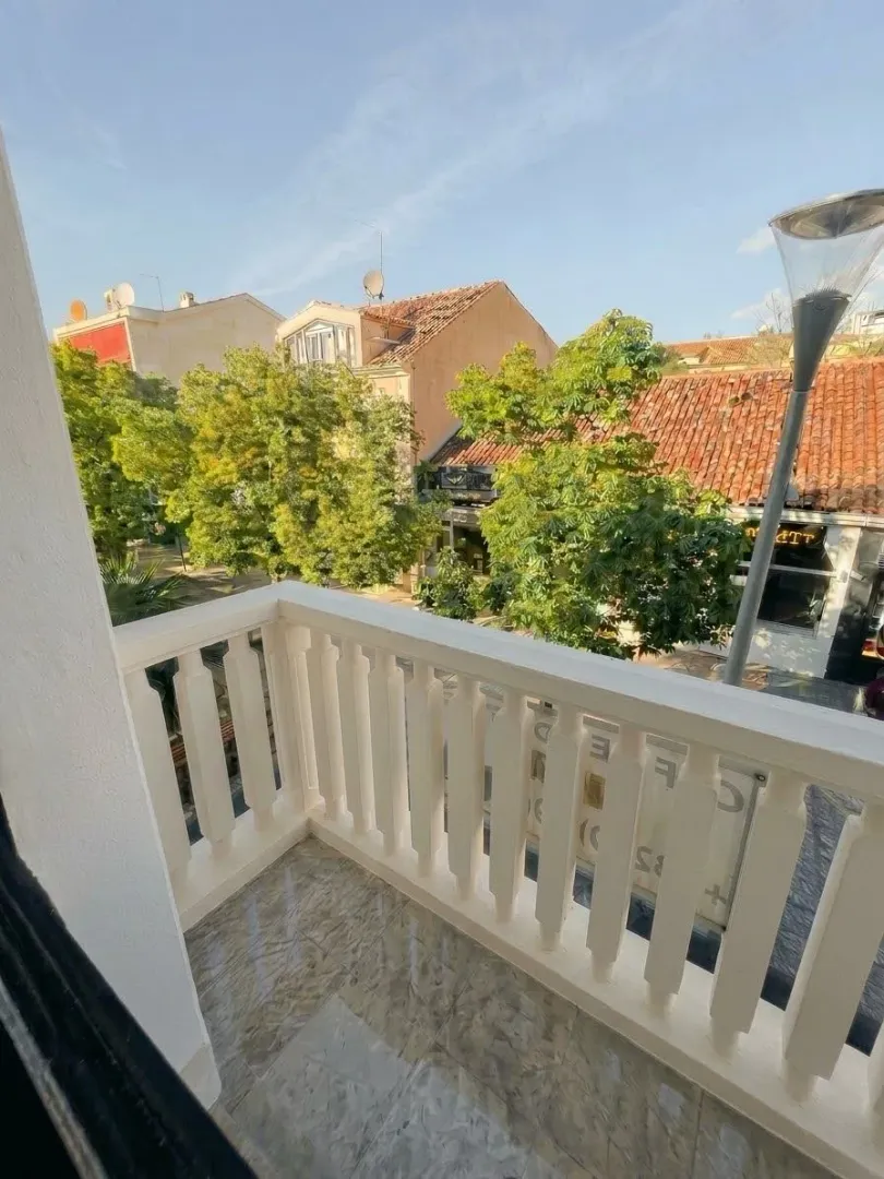 Small bright balcony with a white railing and a city view.