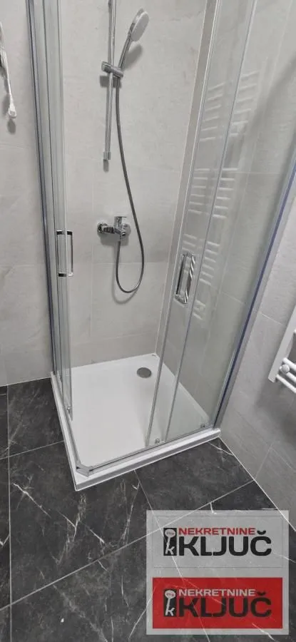Kupatilo sa tuš kabinom i crnim podnim pločicama.